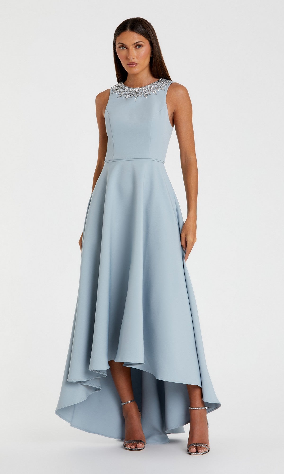 A woman poses against a white background in the Mac Duggal 49844 High-Low Formal Dress in powder blue, featuring an embellished neckline, sleeveless design, elegant A-line skirt, and silver heels.